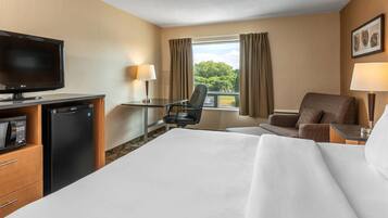 Una habitación de hotel con cama, escritorio con silla, televisión, refrigerador y ventana con cortinas.
