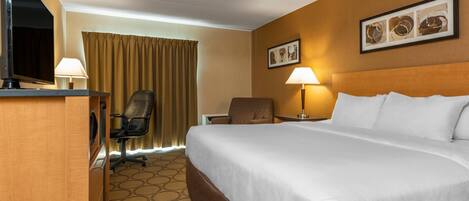 Habitación de hotel con una cama grande, un escritorio con televisor, una silla, una lámpara de escritorio y un cuadro colgado en la pared.