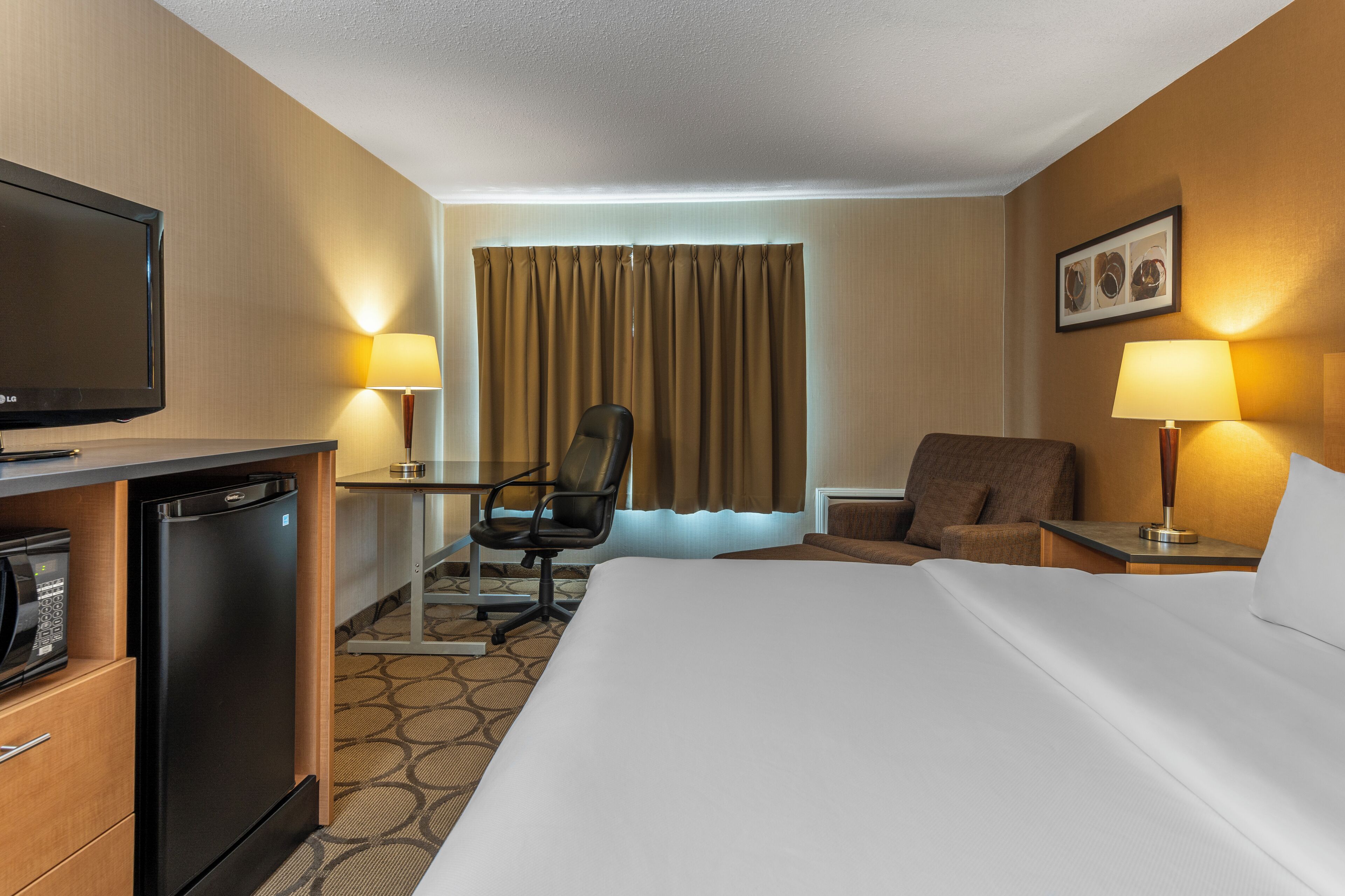 Habitació d'hotel amb llit, escriptori, cadira, televisió i microones.