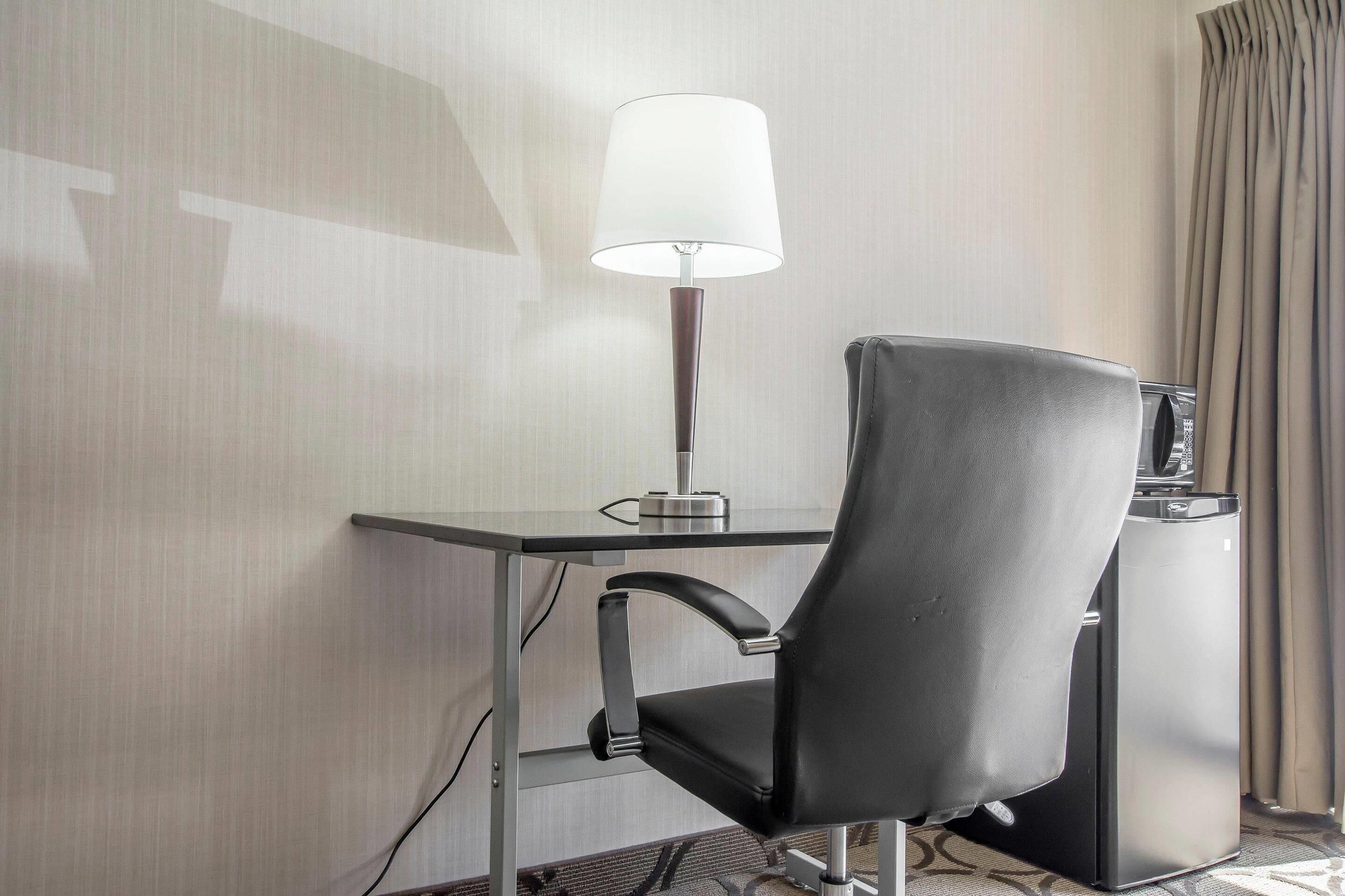 A modern hotel room with a desk, a black leather chair, a lamp, and a minibar.