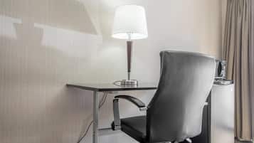 A modern hotel room with a desk, a black leather chair, a lamp, and a minibar.