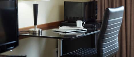 A hotel room with a desk, a television, a microwave, a chair, and a lamp.