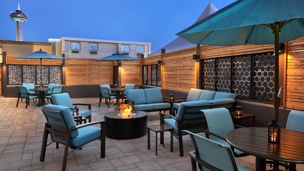 An outdoor seating area with round tables and chairs, a fire pit, and umbrellas providing shade. - Fairfield by Marriott Niagara Falls, Canada (Niagara Falls)
