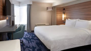 Una habitación de hotel con una cama grande, un escritorio, una silla, un televisor y una lámpara.