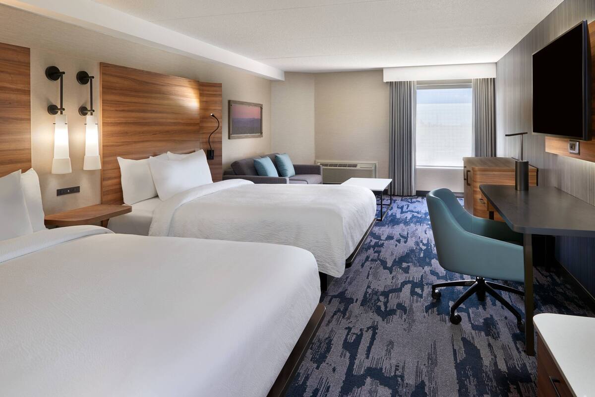 A hotel room with two beds, a desk, a chair, a TV, and a window with curtains.