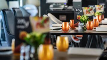 Une scène de restaurant avec un présentoir à menus, des tasses oranges et un ordinateur portable posé sur la table.