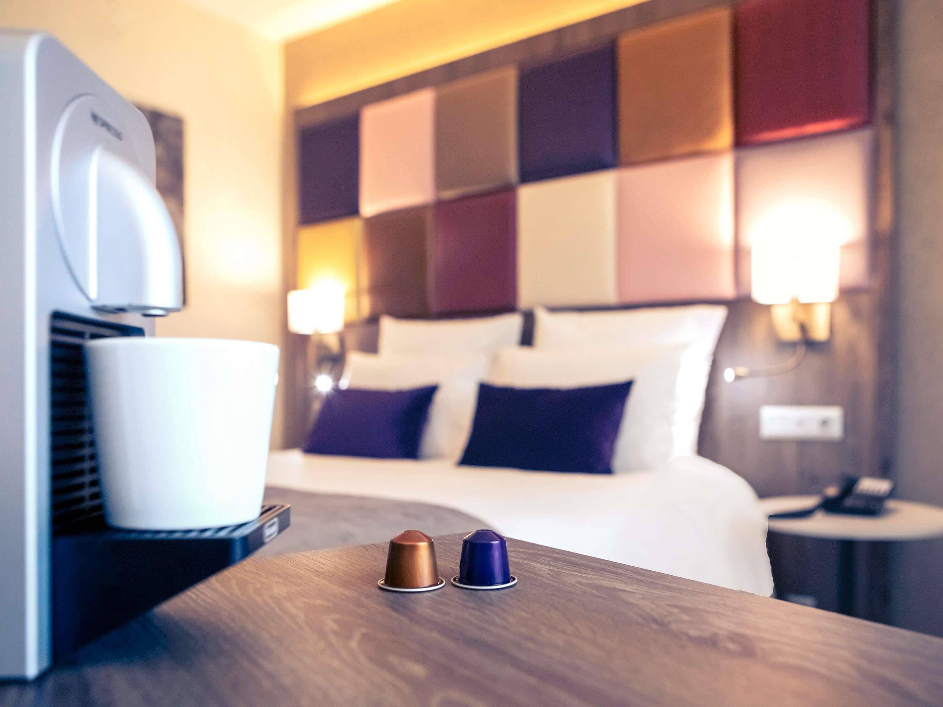 A hotel room with a bed, bedside table, and a coffee machine.