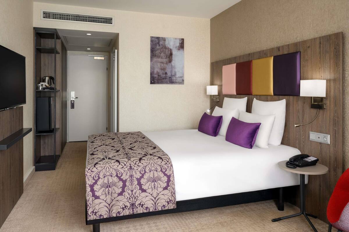 A hotel room with a bed, bedside table, lamp, and a television.