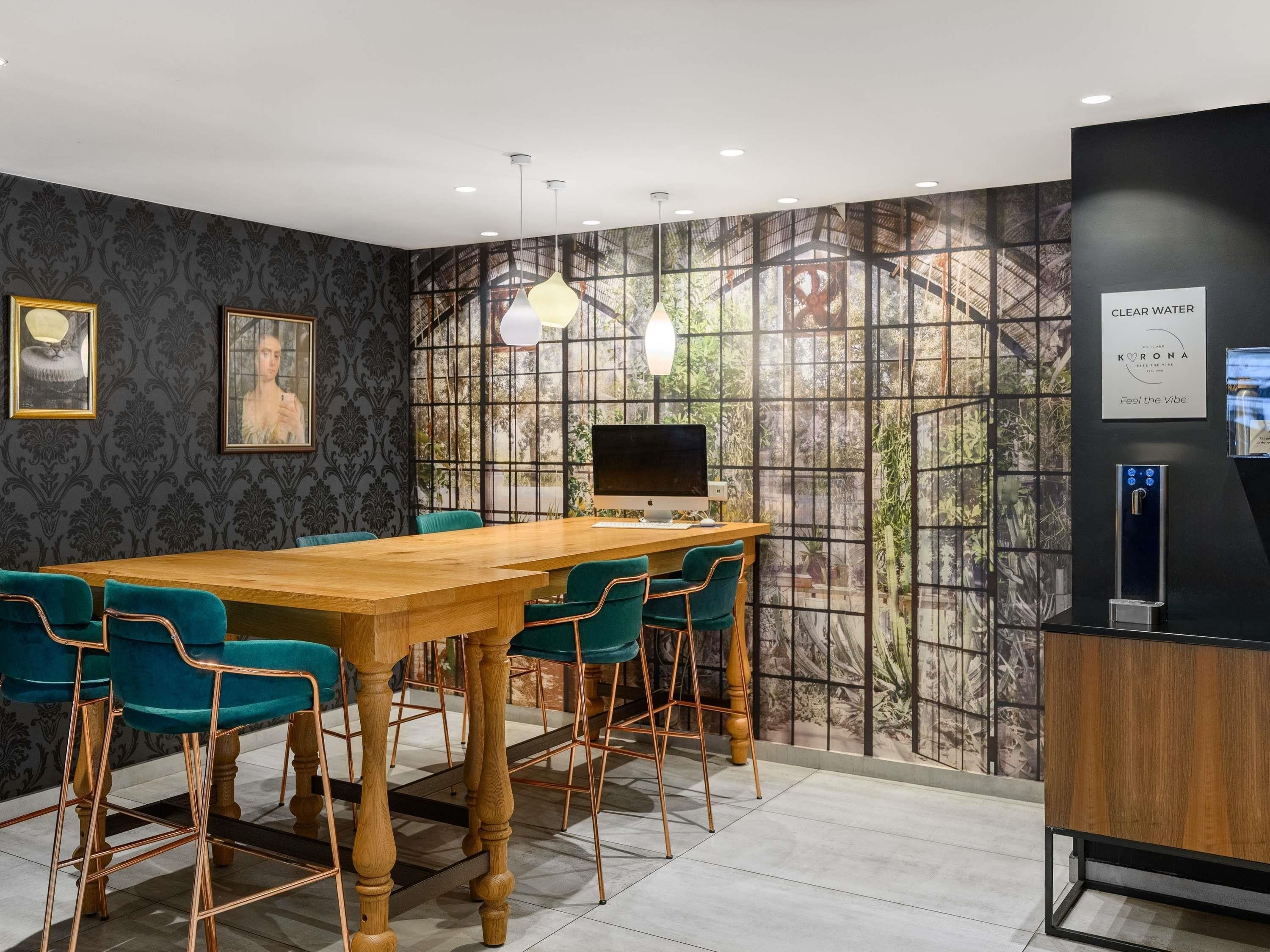 Une salle de conférence avec une longue table en bois, des chaises de couleur turquoise, un ordinateur de bureau et un distributeur d’eau.