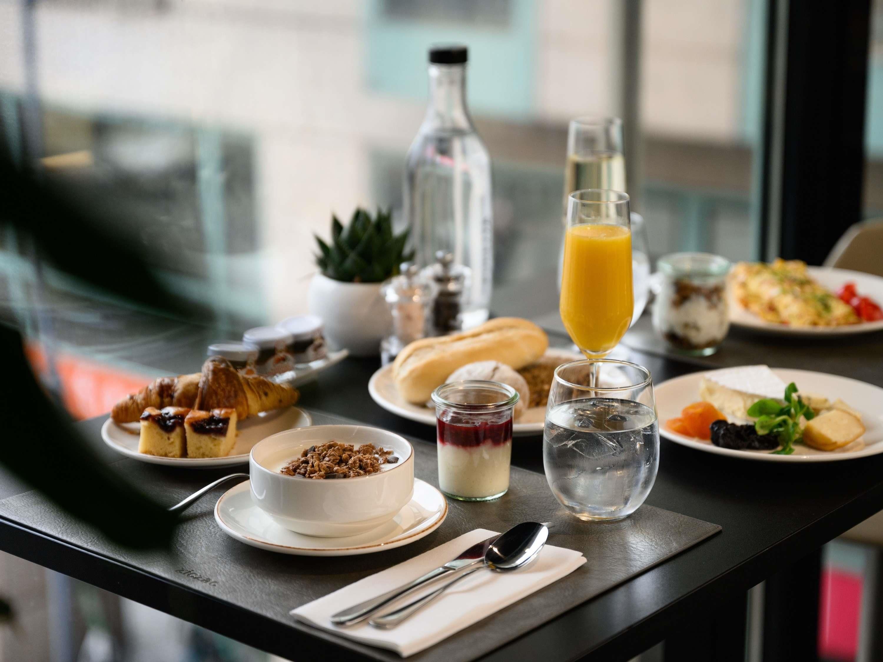A breakfast table with various food items, a glass of orange juice, and a bottle of water.