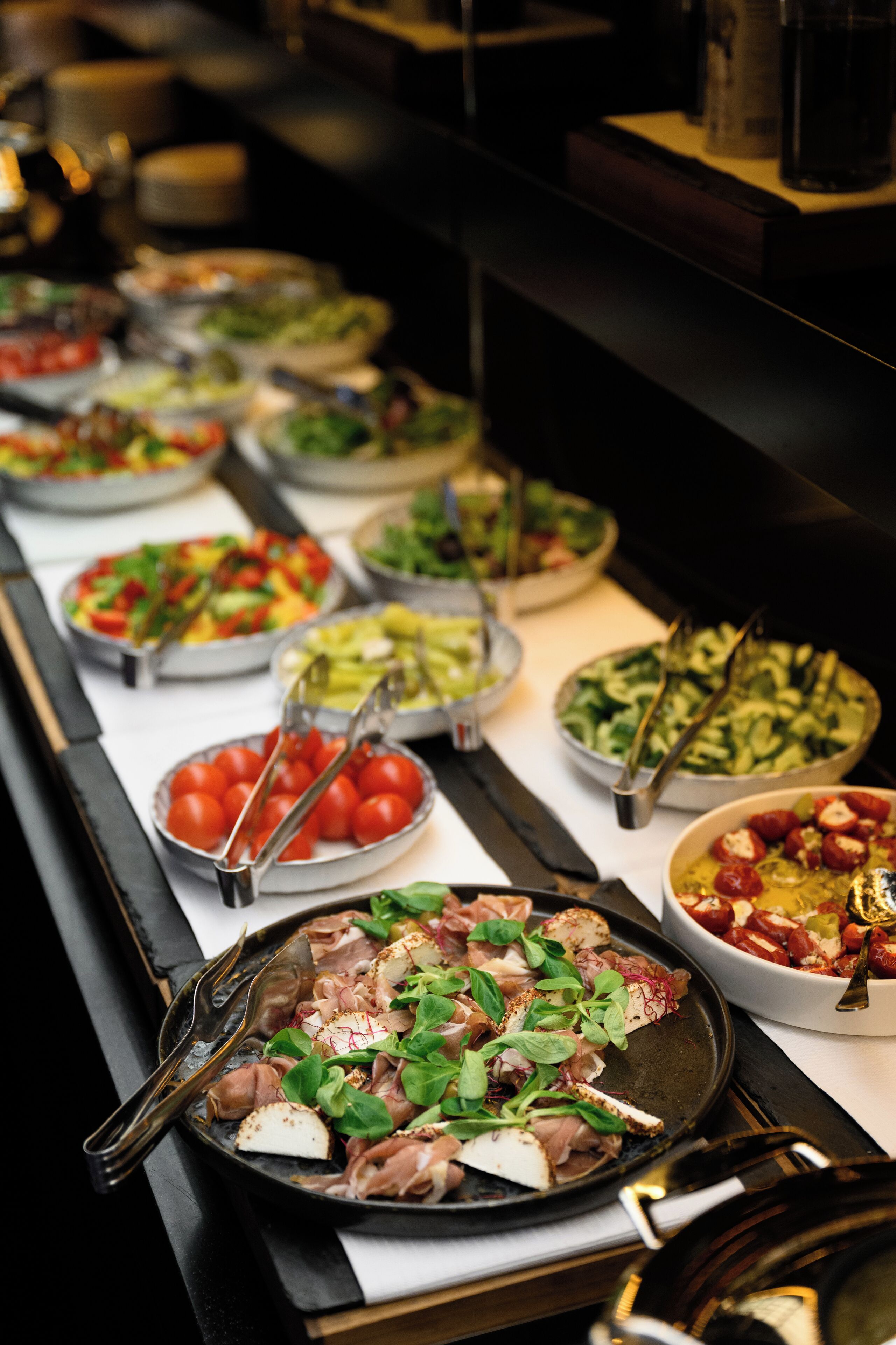 A buffet with various dishes including salads, meats, and cheeses.