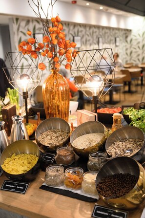 Zona de bufé con diversas opciones de comida y un jarrón decorativo con flores naranjas.