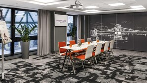 Uma sala de conferências com uma mesa grande, cadeiras, um projetor e um mural da paisagem urbana.