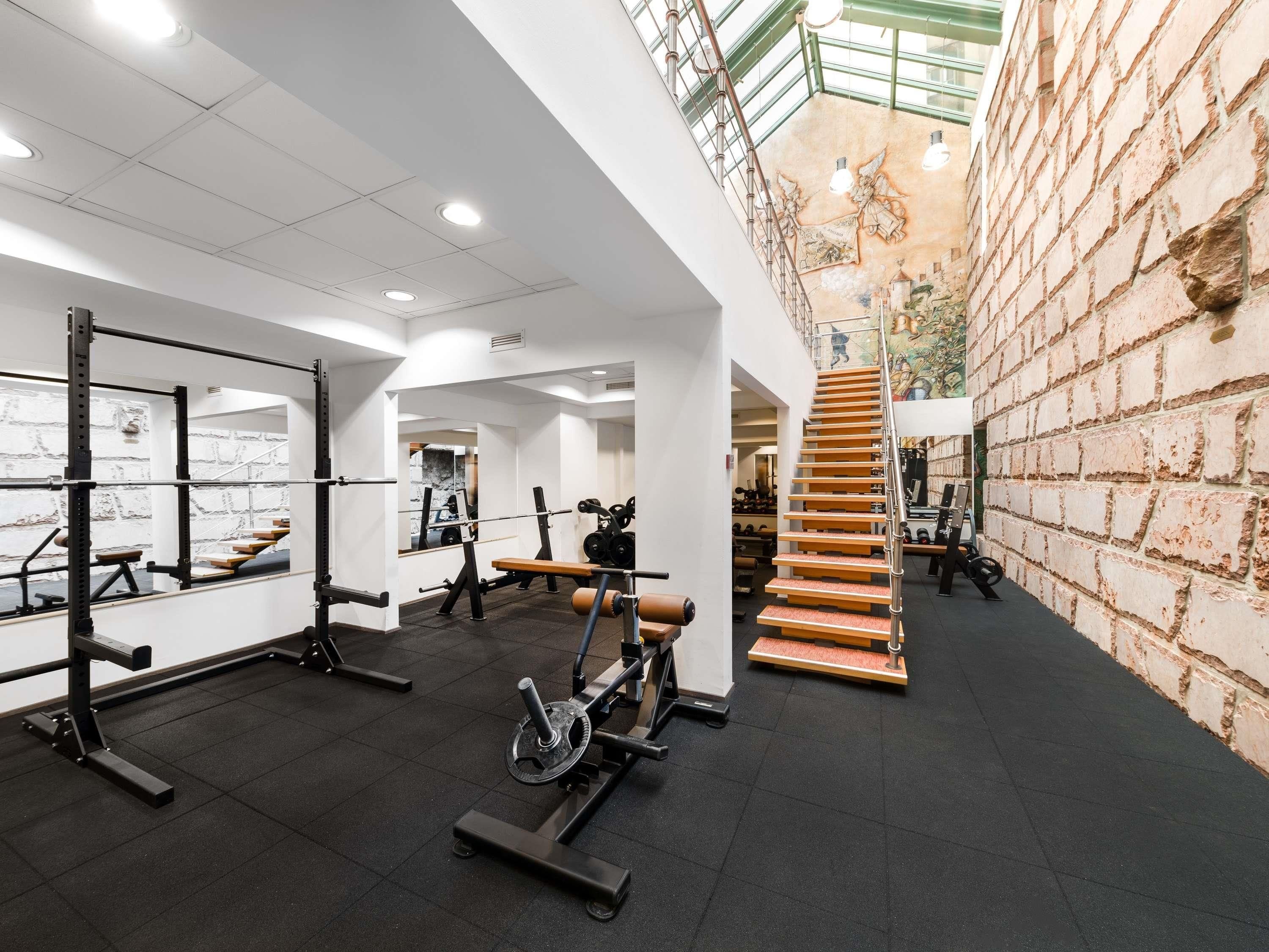 Une salle de sport équipée de matériel de musculation, avec un escalier et un mur en briques.