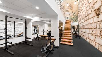 Une salle de sport équipée de matériel de musculation, avec un escalier et un mur en briques.