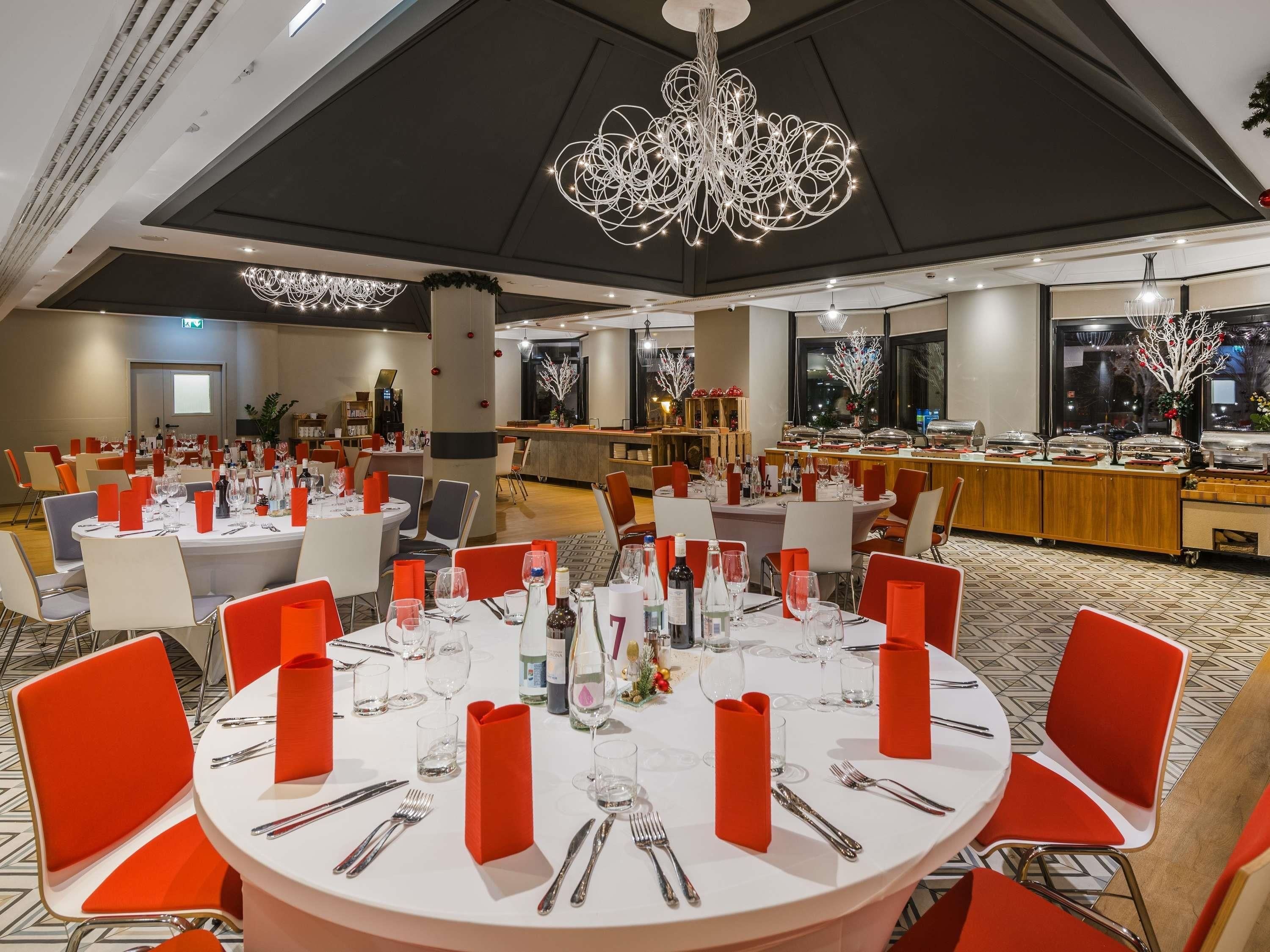 A banquet hall with round tables, red napkins, and a modern chandelier.