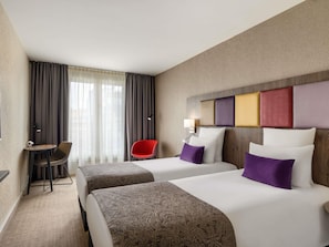 A hotel room with two beds, a desk, a chair, and a window with curtains.