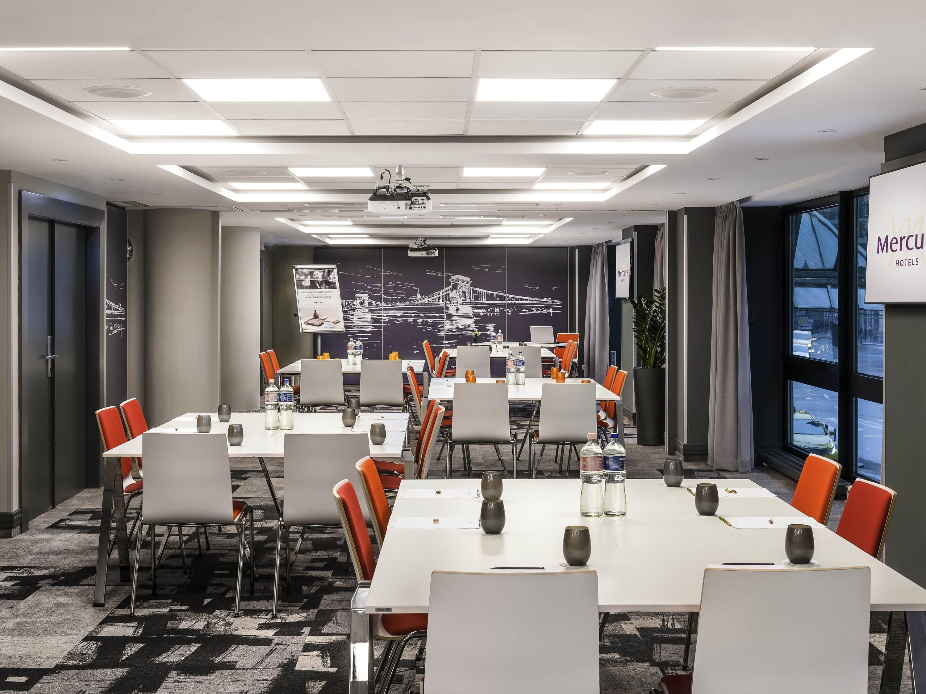 A conference room with tables, chairs, a projector, and a large window with a view.