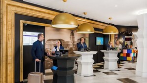 Um hall de hotel com balcões de recepção, uma tela digital grande e um balcão de check-in.
