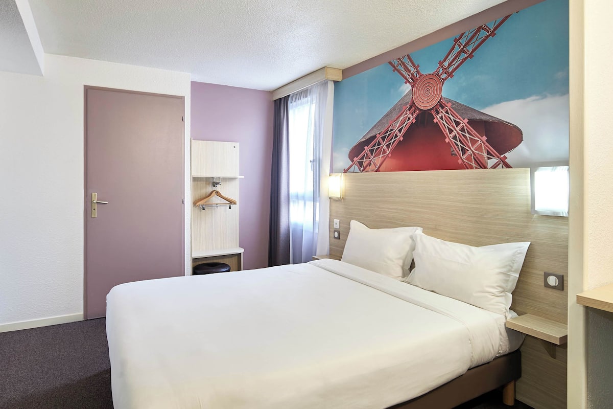 A hotel room with a large bed, a headboard with a mural, a wardrobe, and a nightstand.