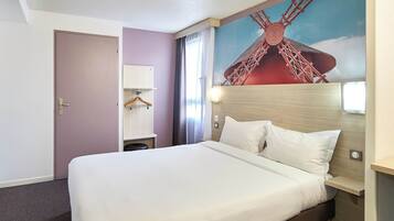 Une chambre d’hôtel avec un grand lit, une tête de lit ornée d’une fresque représentant un moulin, une armoire et une table de chevet.