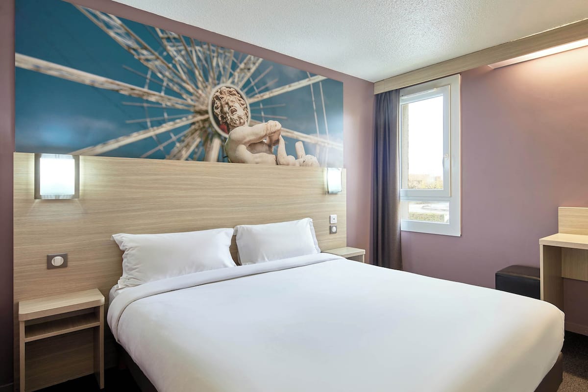 A hotel room with a large bed, two bedside tables, a wall-mounted lamp, and a decorative wall piece.