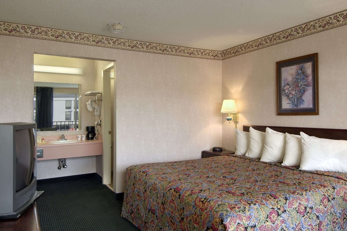 A hotel room with a bed, a television, a bathroom with a sink and mirror, and a painting on the wall.