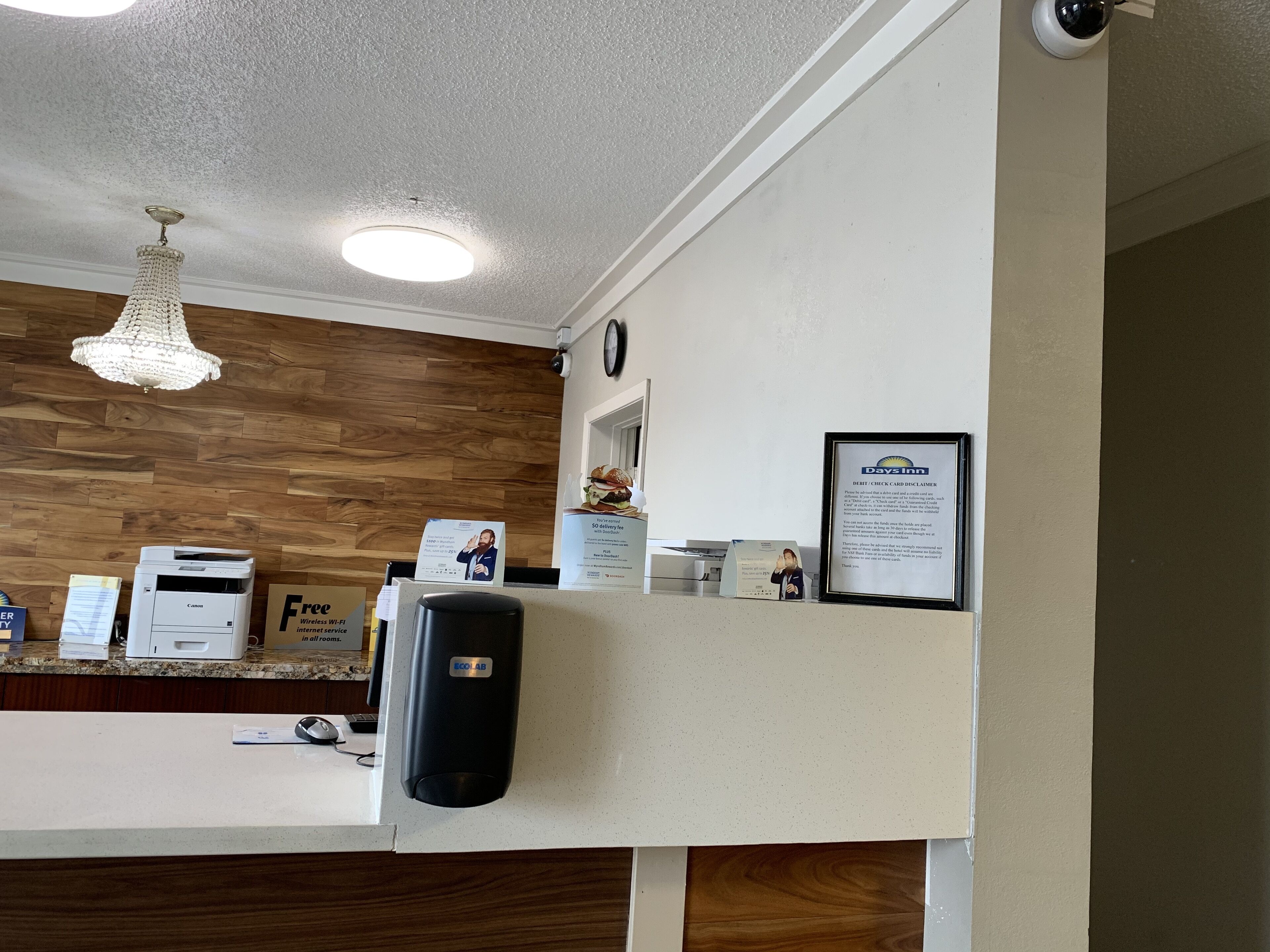 Una recepción de hotel con una pared de madera, una araña, un reloj y un cartel enmarcado.