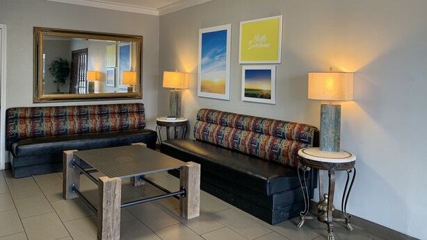 A living room with a sofa, a coffee table, a side table, a lamp, and a mirror. - Days Inn by Wyndham Jonesboro AR (Jonesboro)