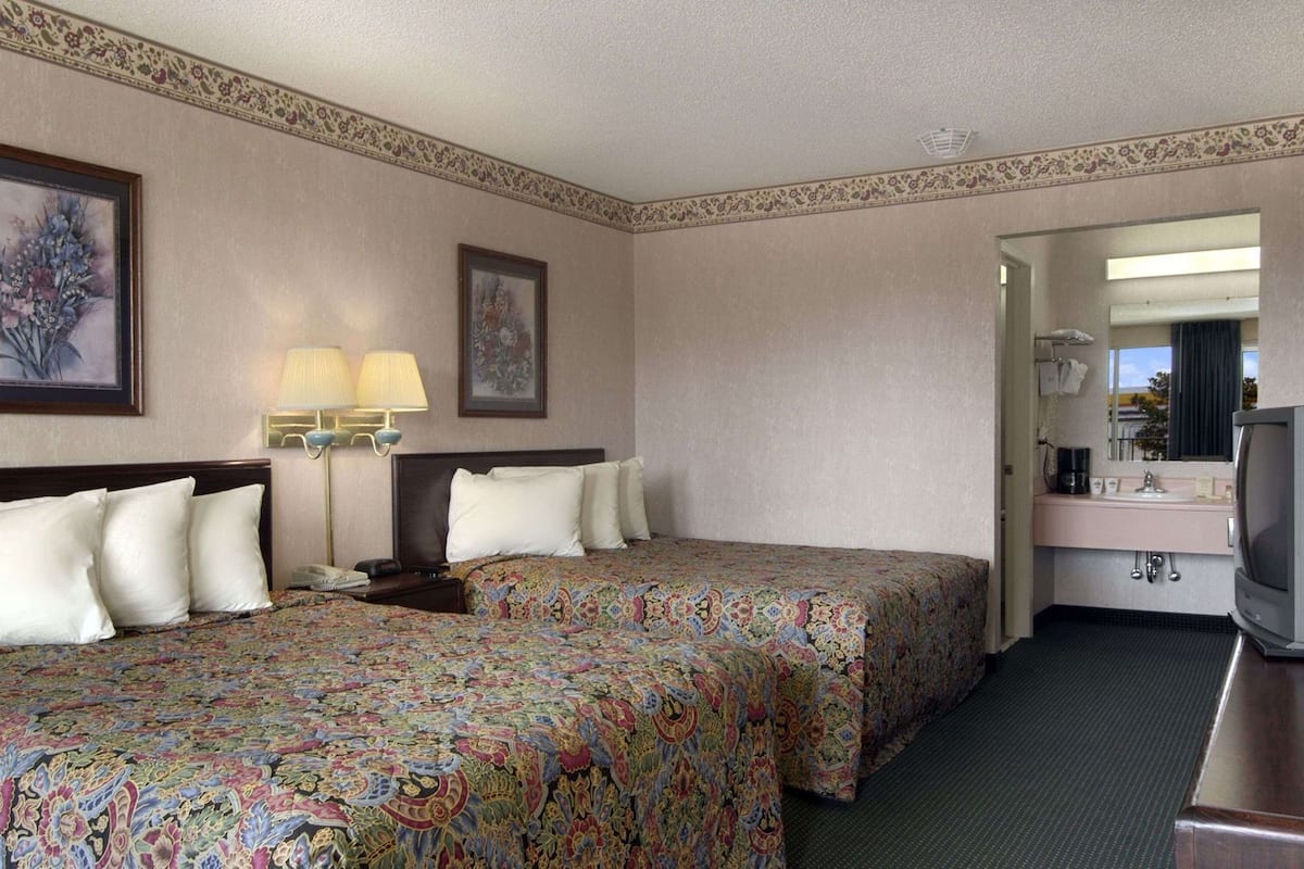 A hotel room with two beds, a desk with a television, a bathroom with a sink and mirror, and a decorative border on the walls.