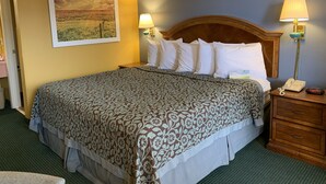 A hotel room with a large bed, two bedside lamps, a wooden headboard, a nightstand with a phone and a clock, and a framed landscape painting on the wall. - Days Inn by Wyndham Jonesboro AR (Jonesboro)