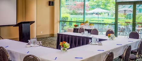 A conference room with a long table, chairs, a podium, and a large window with a view of greenery.