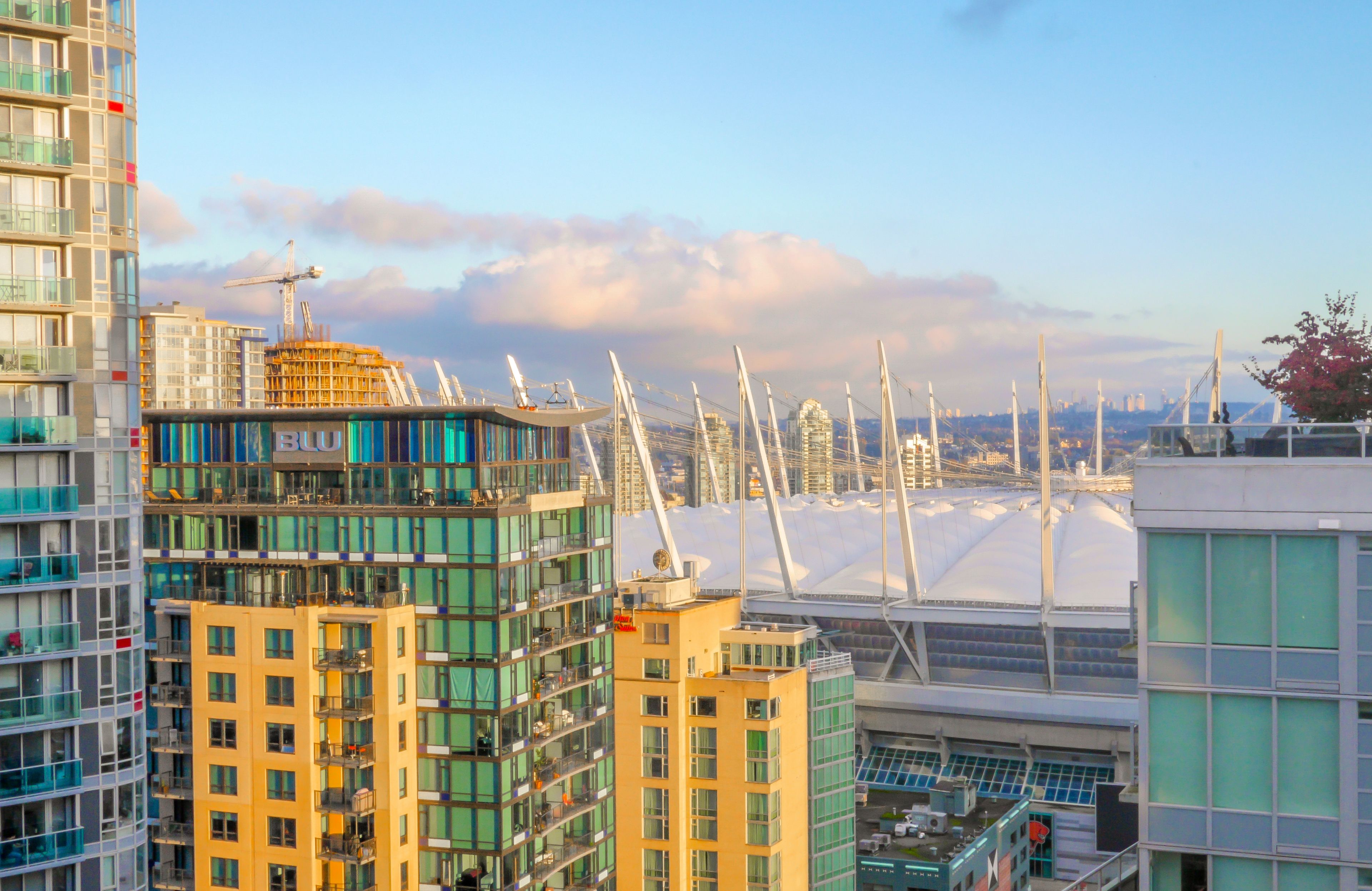 A modern urban skyline with high-rise buildings, a distinctive bridge with white cables, and a construction crane in the background.