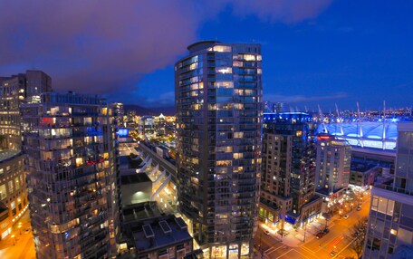 A high-rise building with multiple floors, surrounded by other buildings, and a view of a cityscape at night.