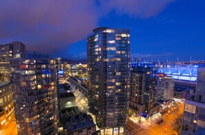 Un edificio alto con varios pisos, rodeado de otros edificios, y una vista del paisaje urbano de noche.