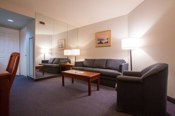 Una habitación de hotel con sofá, sillón, mesa de centro de madera y una lámpara.