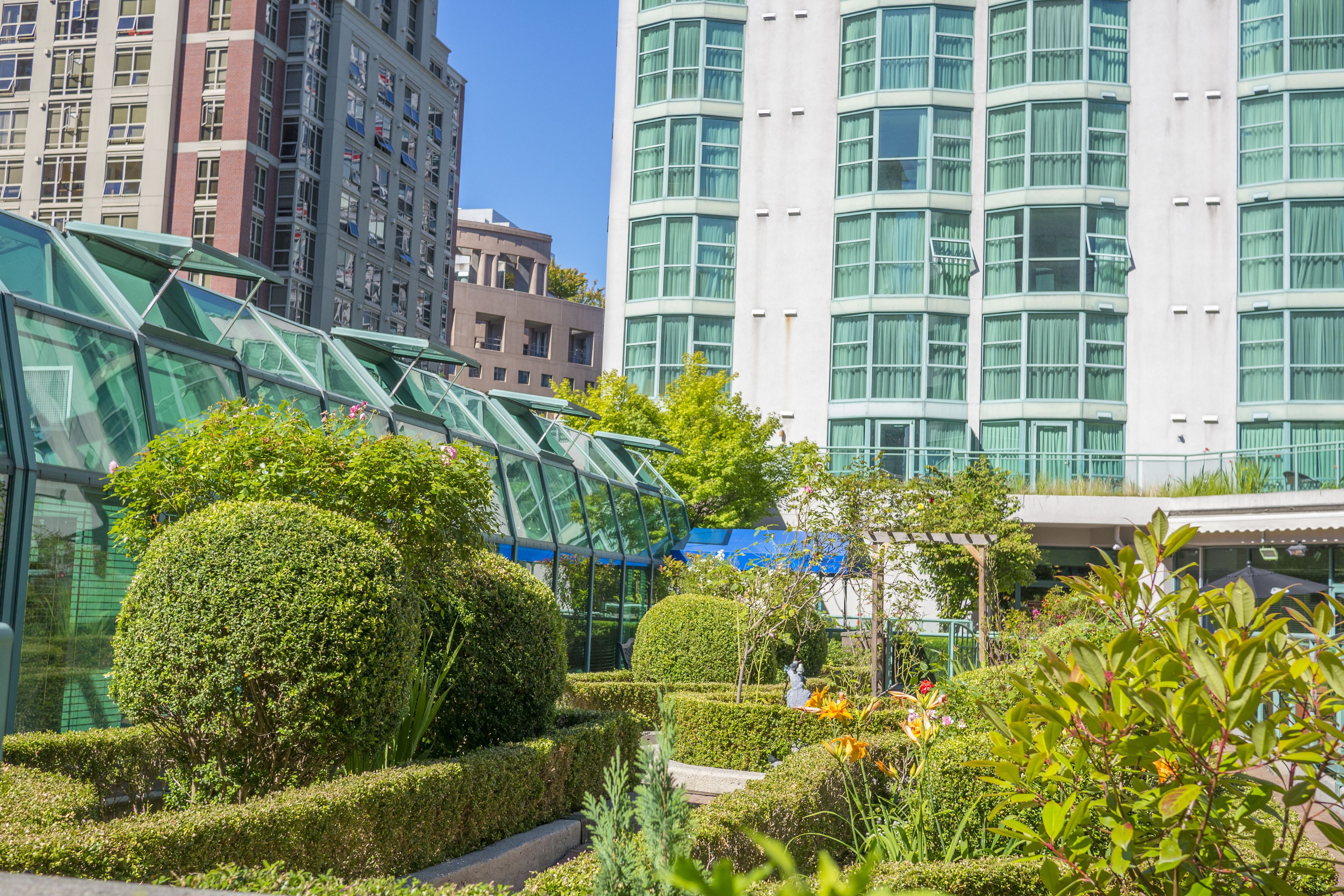 Un bâtiment moderne doté d’une façade en verre et d’un jardin bien entretenu, agrémenté de diverses plantes et d’une statue.