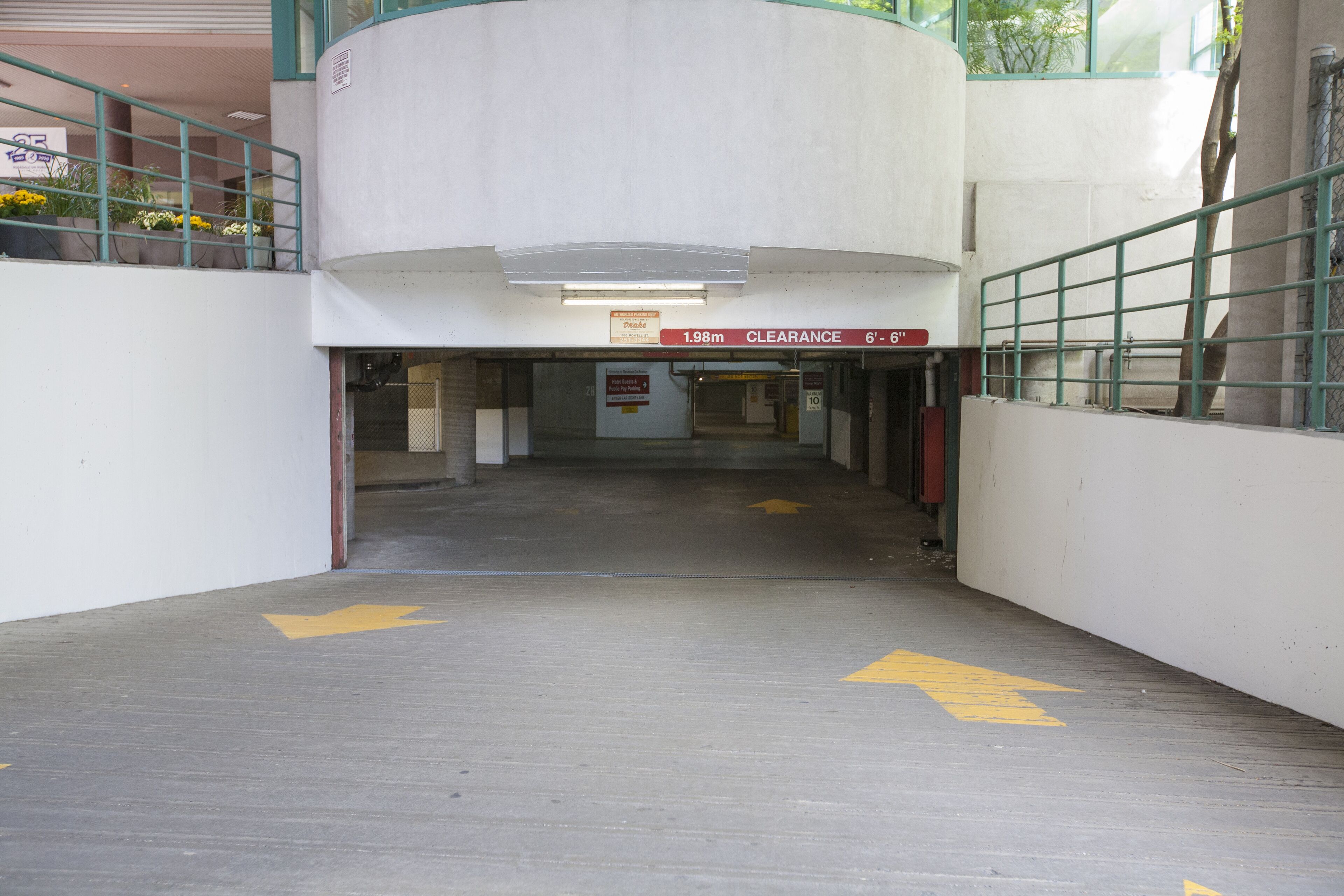 A corridor with directional arrows on the floor, a sign indicating a clearance height of 1.98m, and a staircase with a green railing.