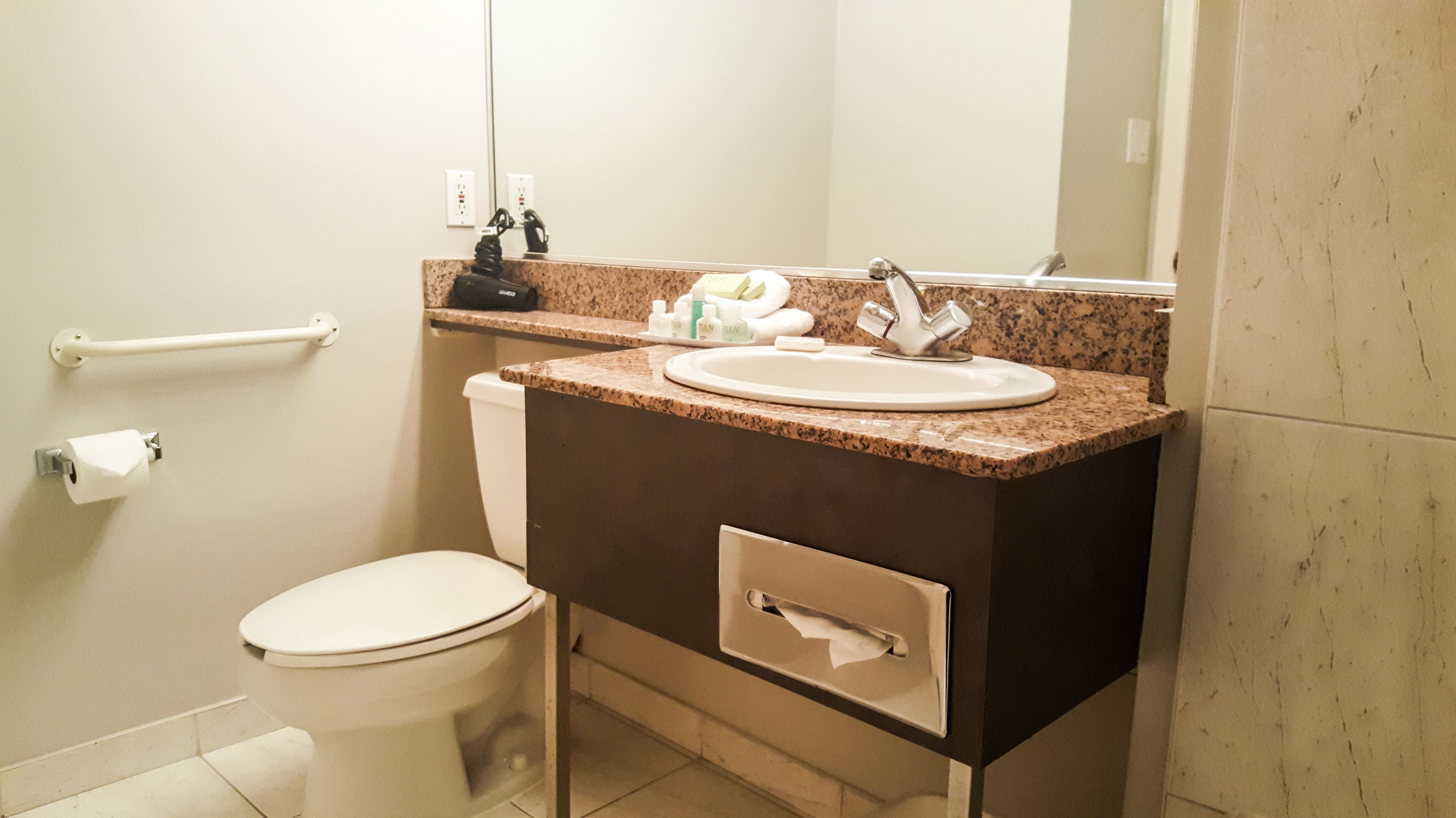 A bathroom with a toilet, sink, mirror, towel rack, and a trash bin.