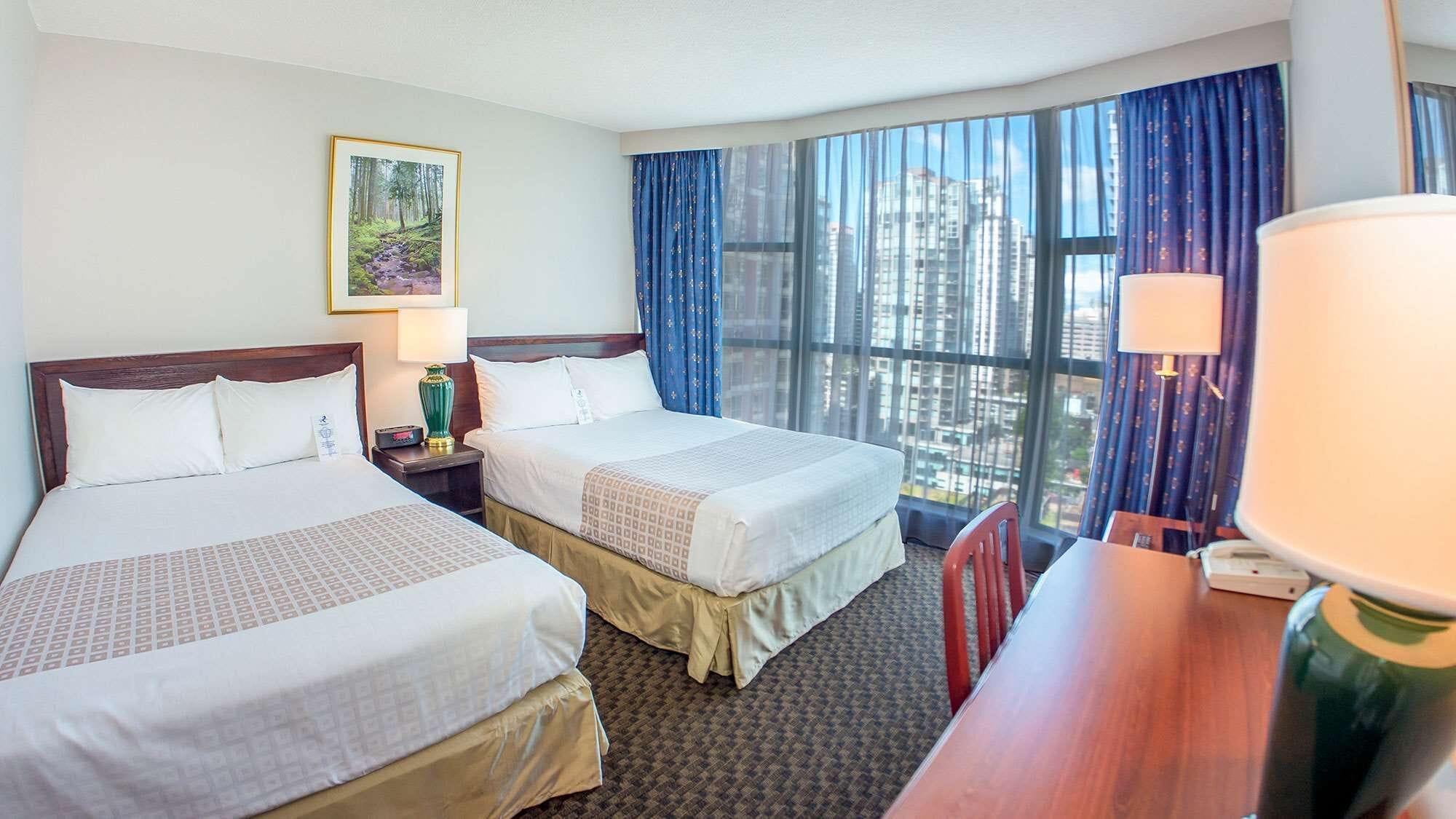A hotel room with two beds, a desk, a chair, a lamp, and a large window with curtains.
