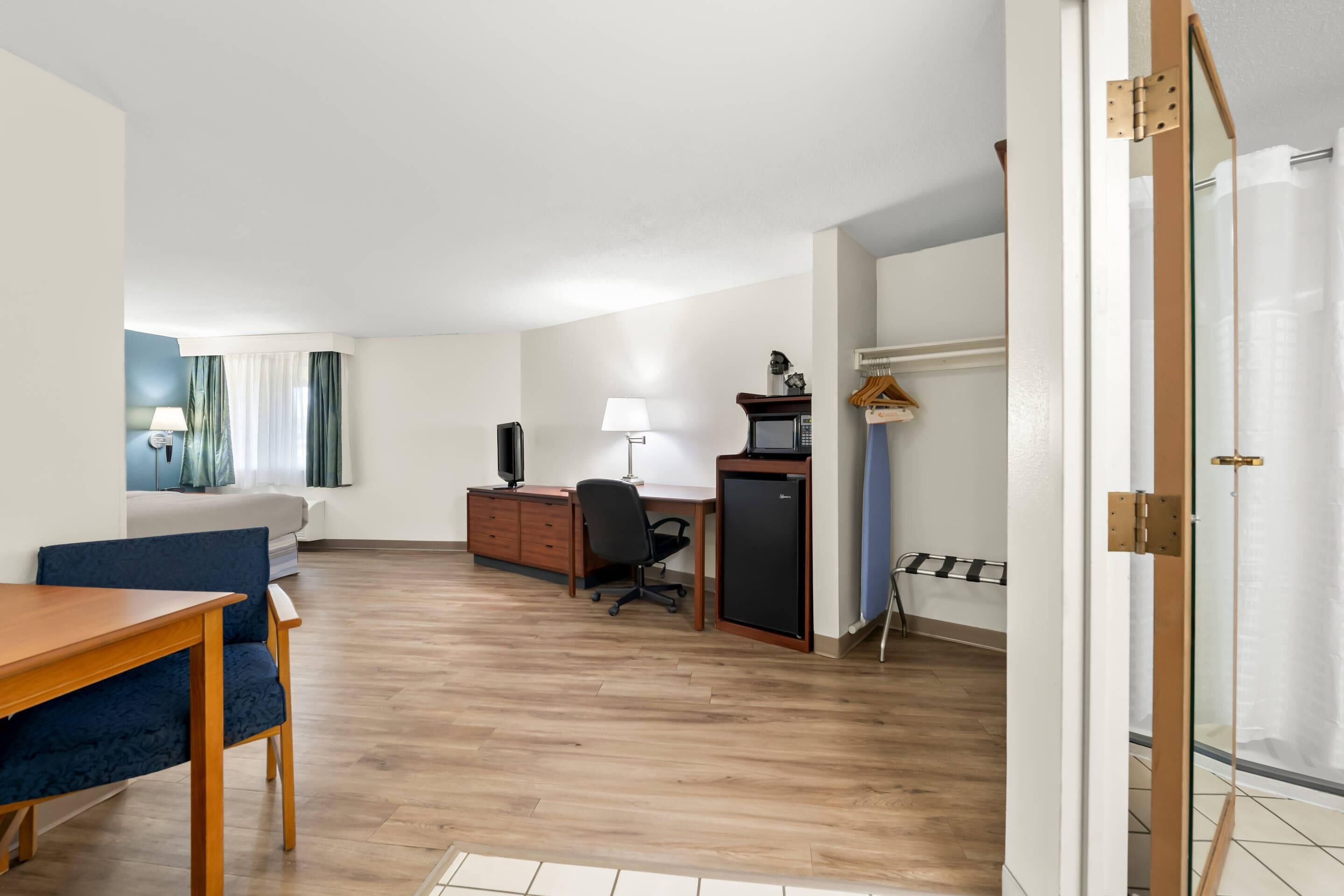 A hotel room with a wooden floor, a desk with a computer, a chair, a bed, and a TV.