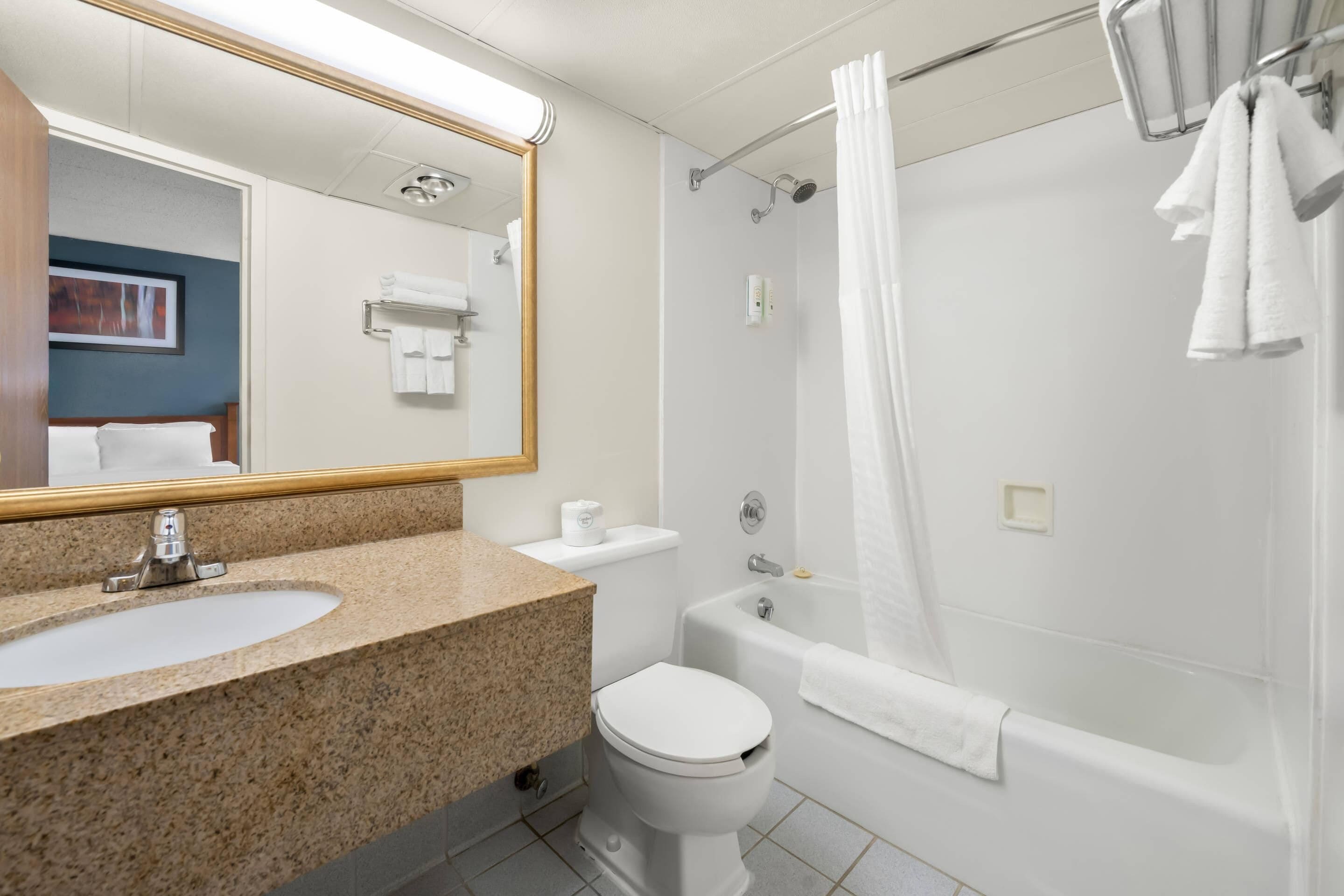 A bathroom with a granite countertop sink, a white toilet, a bathtub, and a shower curtain.