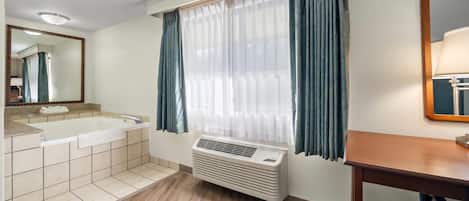 Un bany amb banyera, mirall, finestra amb cortines i un radiador.