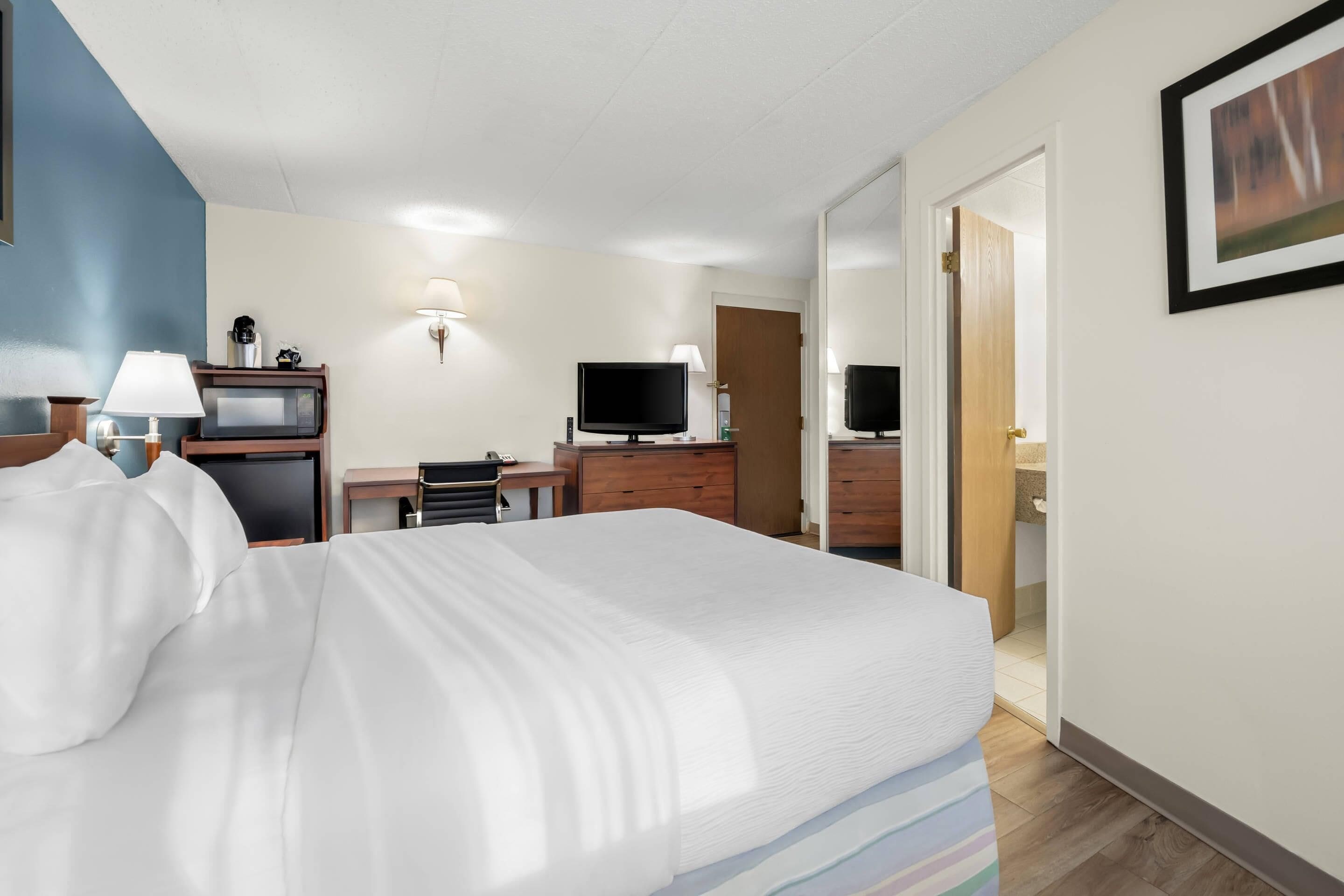 A hotel room with a bed, a desk with a computer, a TV, and a lamp.