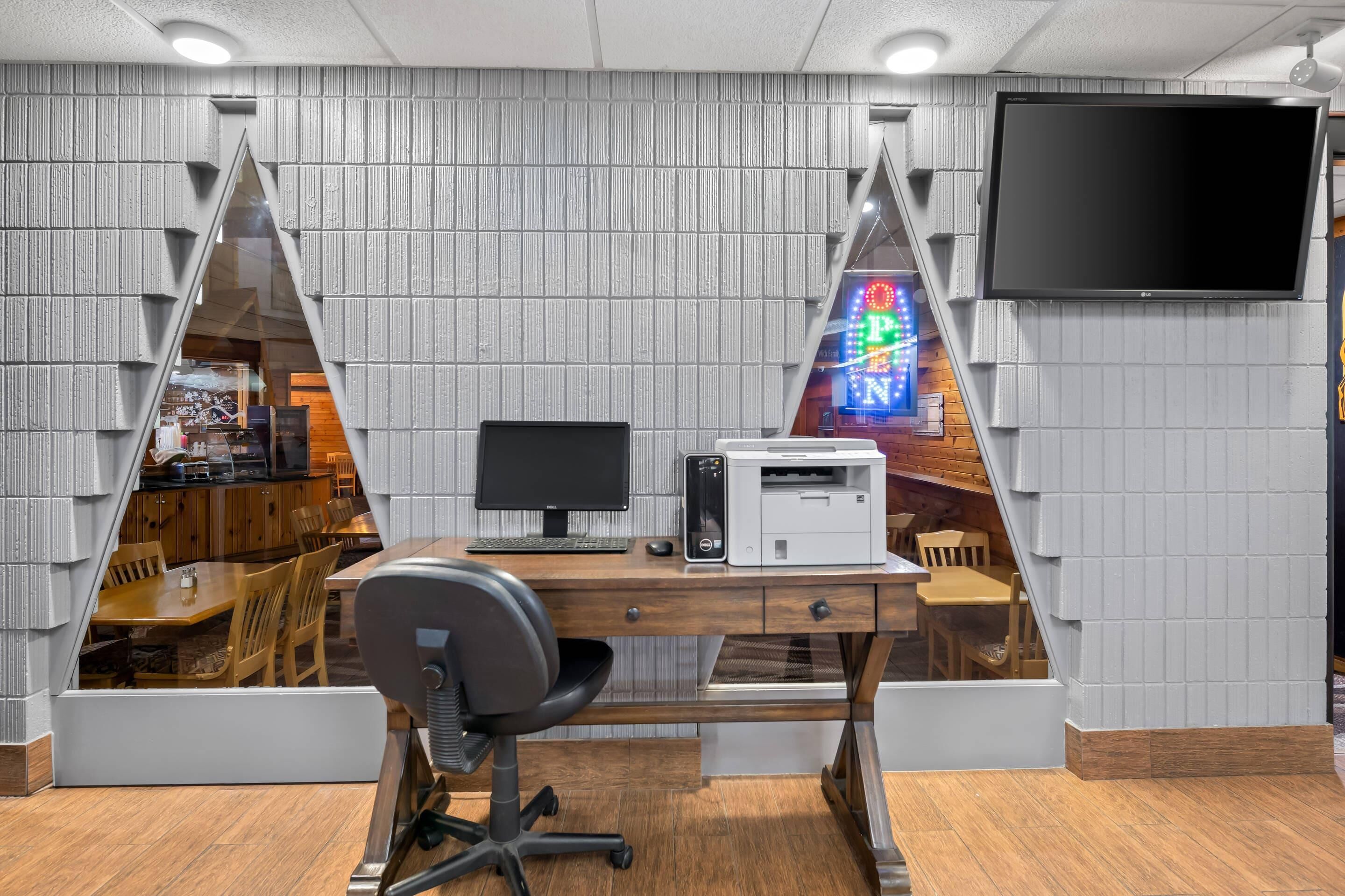 Et moderne kontor med et skrivebord, computer, printer og et fjernsyn ophængt på væggen.
