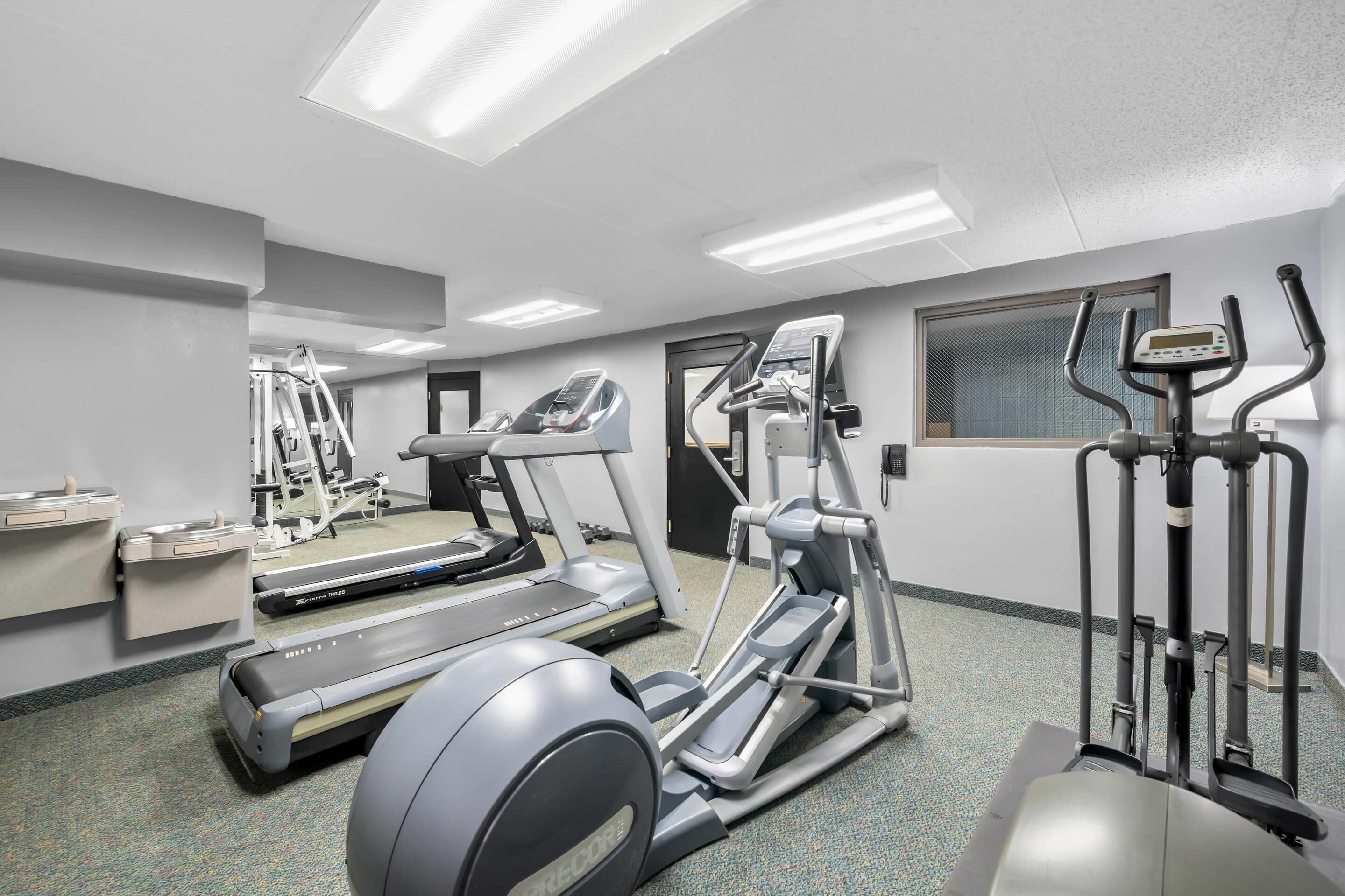 A fitness center with treadmills, elliptical machines, and a mirrored wall.