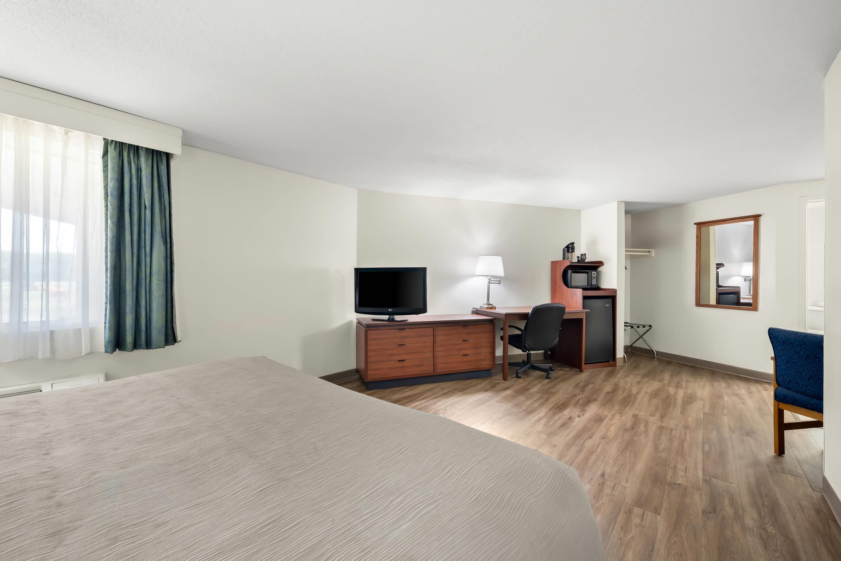 A hotel room with a large bed, a desk with a computer, a television, a chair, and a mirror.