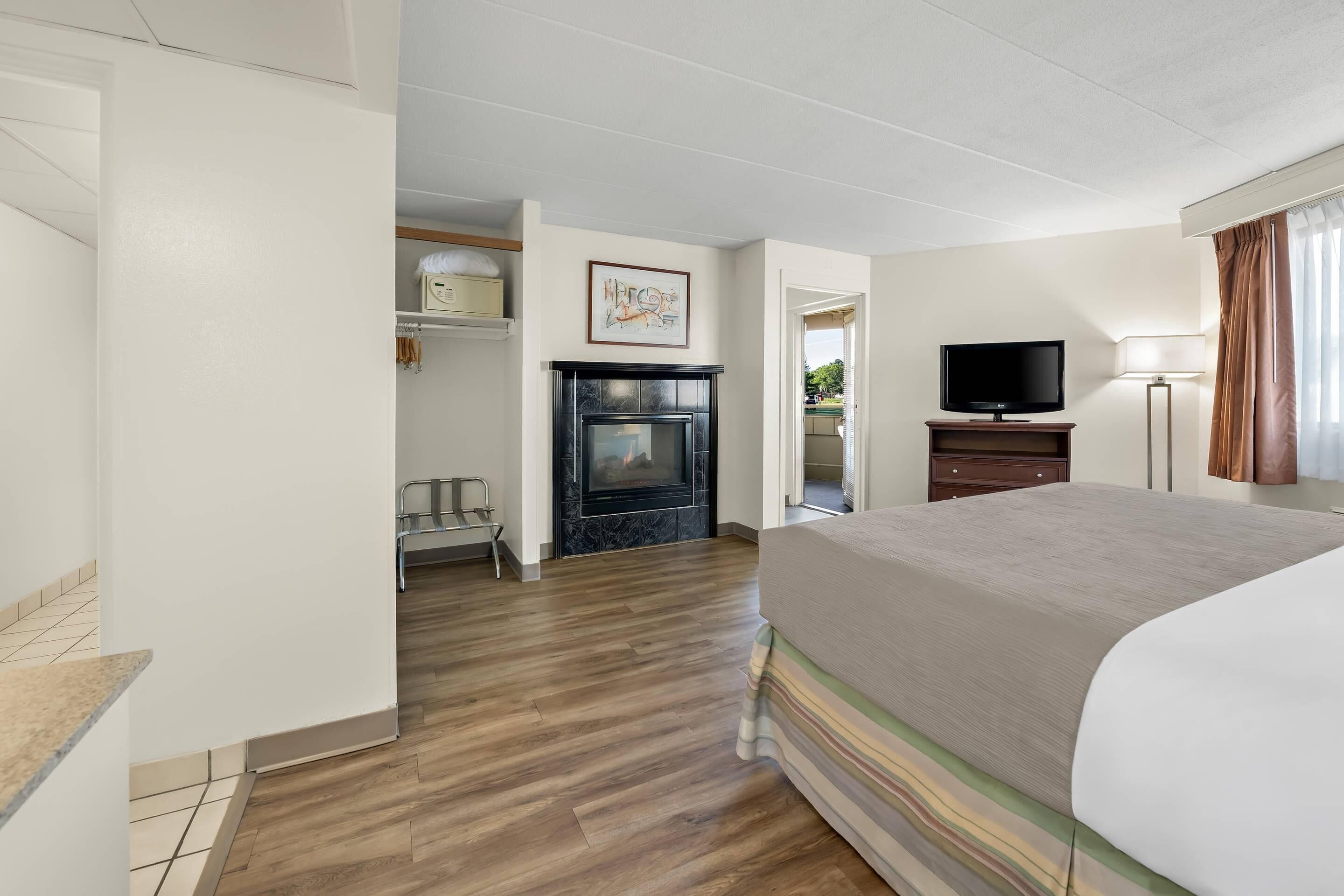 A hotel room with a bed, a television, a fireplace, and a hallway leading to another room.