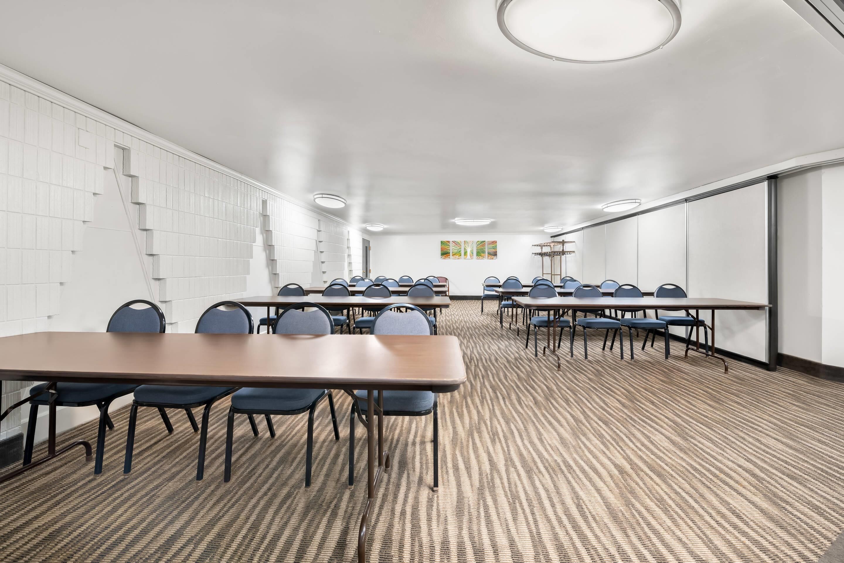 A conference room with a long table, chairs, carpeted floor, white walls, and ceiling lights.