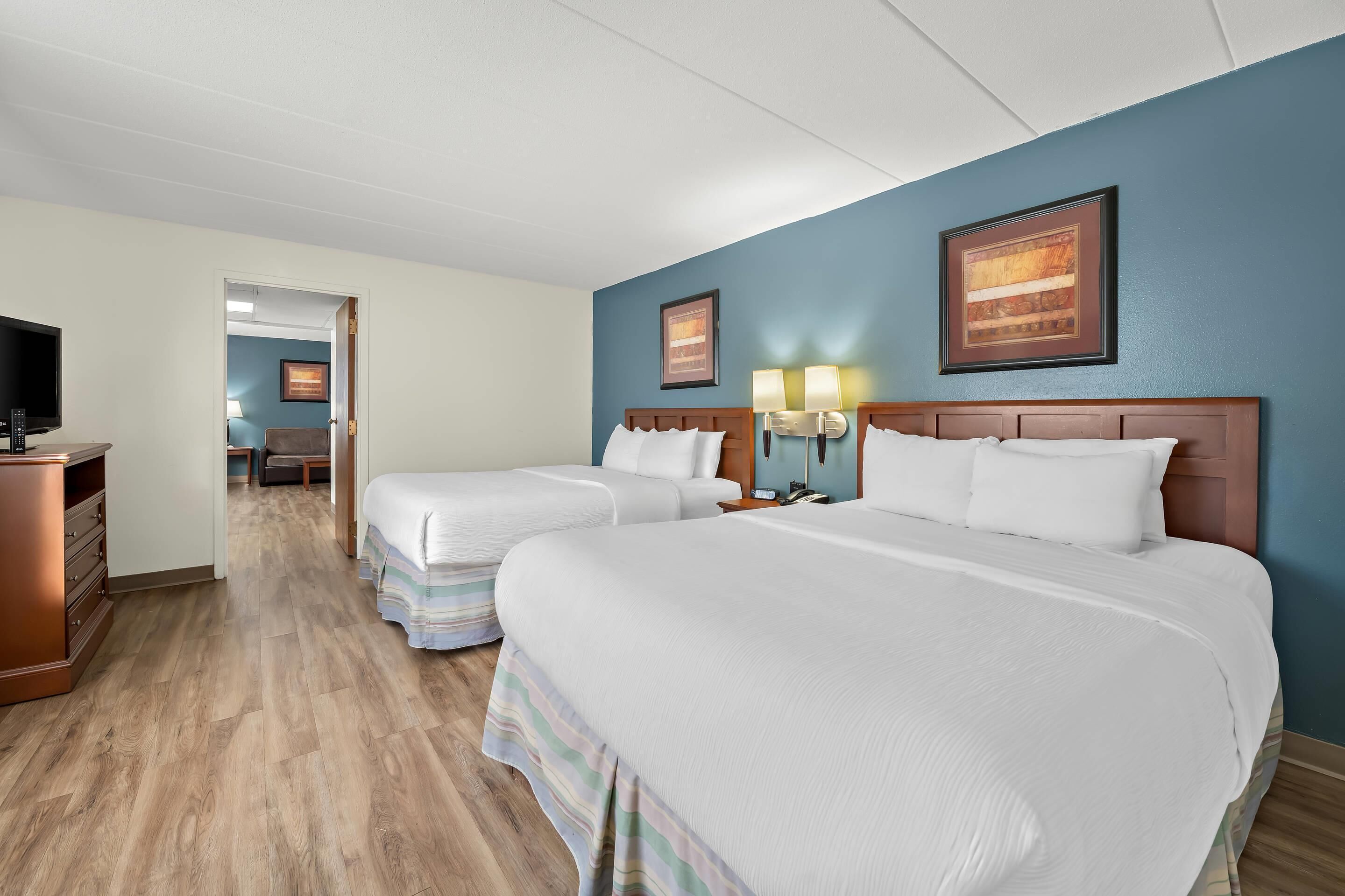 A hotel room with two beds, a TV, a desk, and a bathroom visible through an open door.